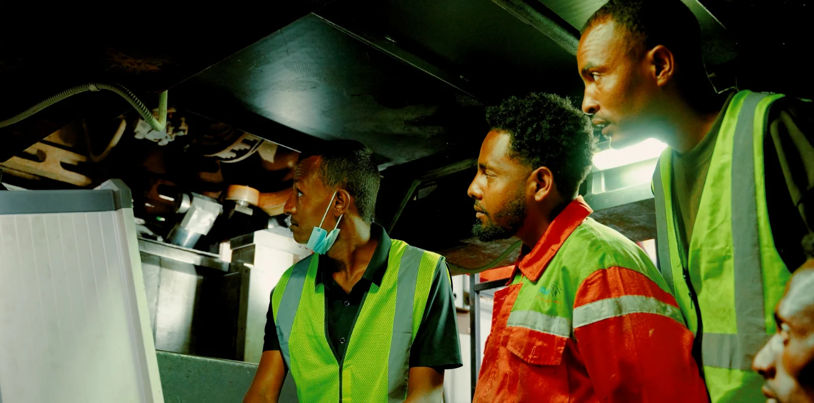 Three EDR staff in high-visibility vests examining the machinery under a passenger coach