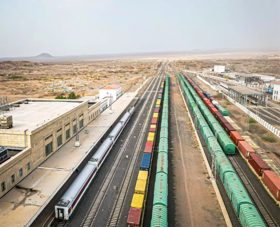 Looking down on a station: a passenger train at the platform and long rakes of freight wagons in the yard beyond