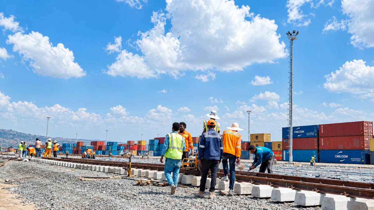 EDR crews laying track across a container yard, with stacks of shipping containers and floodlight masts behind them